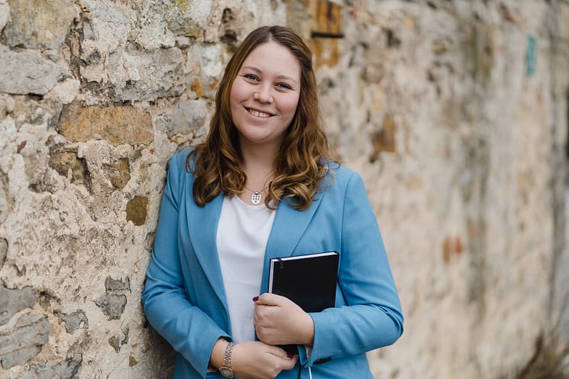 Businessportrait einer lächelnden Frau mit Notizbuch vor einer Natursteinwand in Stuttgart – fotografiert von Kai Schwab